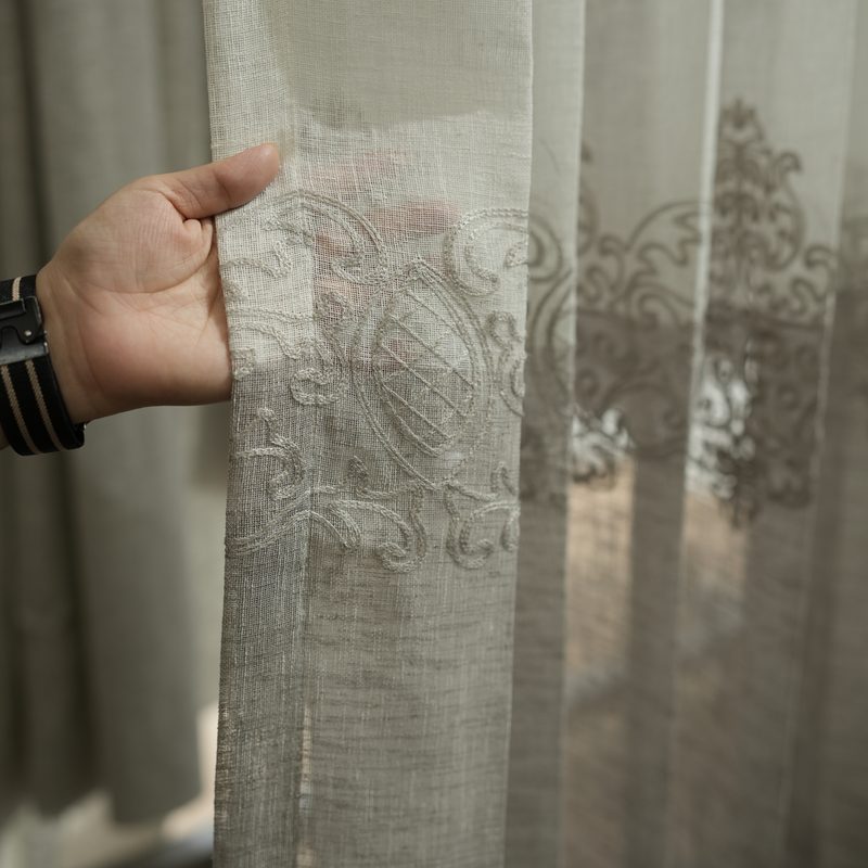Hand holding an embroidered sheer curtain at Drape Shoppe