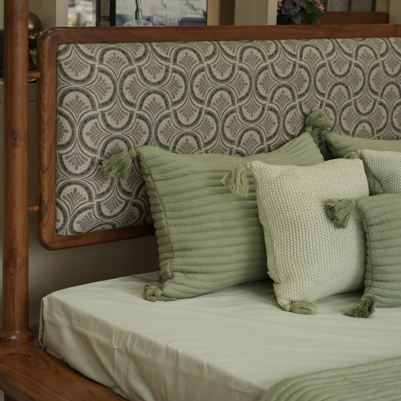 Sage green bedding and cushions on a bed with a patterned headboard at Drape Shoppe